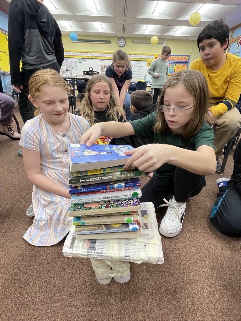 4th-graders Maleah Felton, Delilah Montenary, and Danny Frey watch as Sierra Mason stacks books on their table